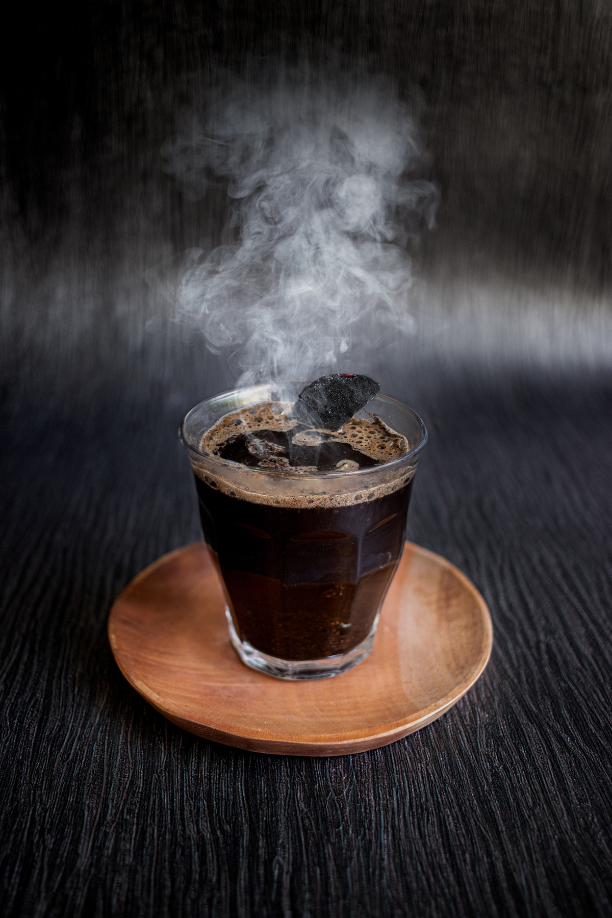 Traditional Black Coffee Kopi Jos with Hot Charcoal Inside on Wooden Plate